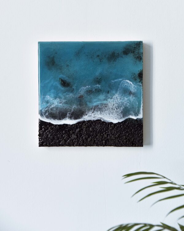 Cuadro realista hecho con resina epoxy sobre panel de madera, recreando una vista aérea de una playa volcánica de arena y rocas negras. El mar se presenta en tonos azules turquesas, con un asombroso efecto de espuma que imita el romper de las olas.