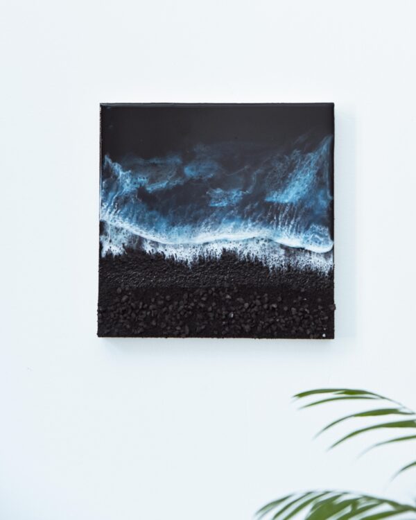 Cuadro realista hecho con resina epoxy sobre panel de madera, recreando una vista aérea de una playa volcánica de arena y mar negro. El mar se presenta en tonos azules turquesas, con un asombroso efecto de espuma que imita el romper de las olas.