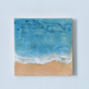 Cuadro realista hecho con resina epoxy sobre panel de madera, recreando una vista aérea de una playa de arena dorada. El mar se presenta en tonos azul turquesa, con un asombroso efecto de espuma que imita el romper de las olas.